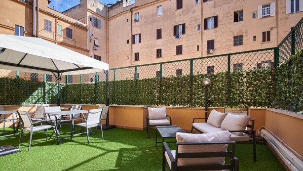 Une terrasse extérieure avec un revêtement de gazon synthétique, des sièges et un parasol blanc.