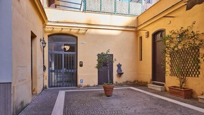 Une cour avec un sol carrelé, une porte, un pot de fleurs et une petite statue.