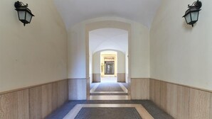 Un couloir doté d’un sol carrelé, de deux appliques murales et d’une arche menant à une porte.