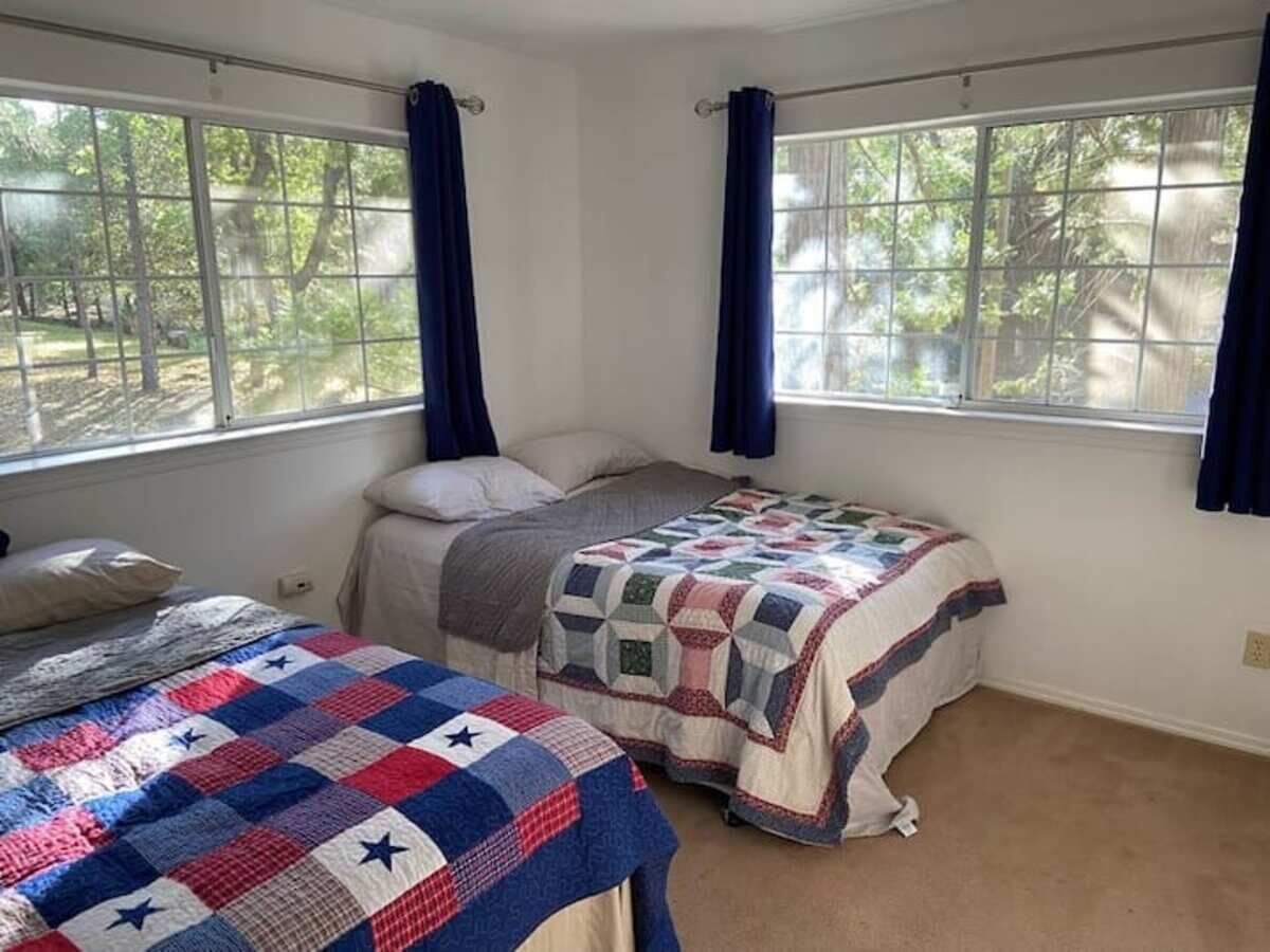 A bedroom with two beds, a large window with curtains, and a view of trees outside.