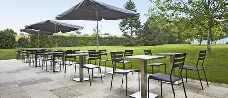 Une terrasse extérieure dotée de plusieurs tables et chaises, protégée par de grands parasols.