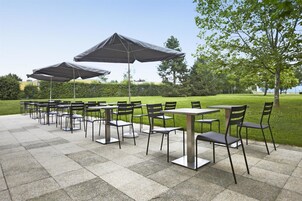 Un patio al aire libre con varias mesas y sillas, cubierto por grandes sombrillas.