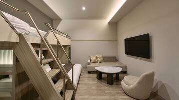 A modern room with a bunk bed, a sofa, a coffee table, and a TV mounted on the wall.