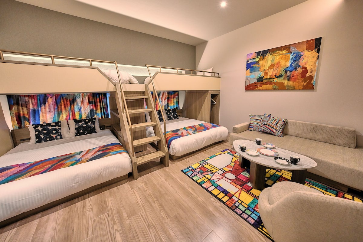 A modern, compact room with bunk beds, a sofa, a coffee table, and a colorful abstract painting.