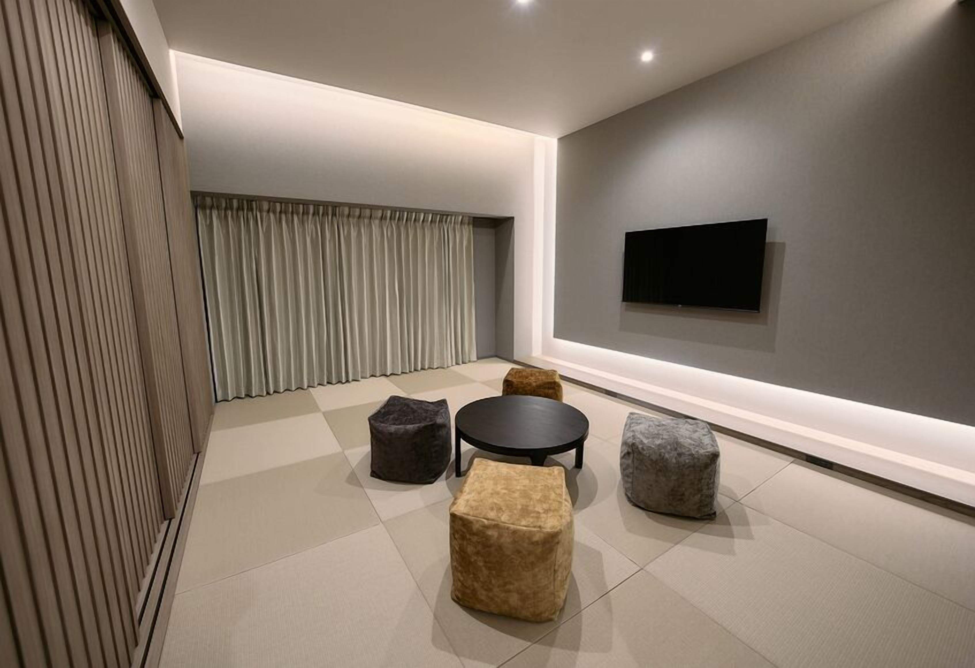 A modern living room with a flat-screen TV mounted on the wall, a round coffee table, and four ottomans in different colors.