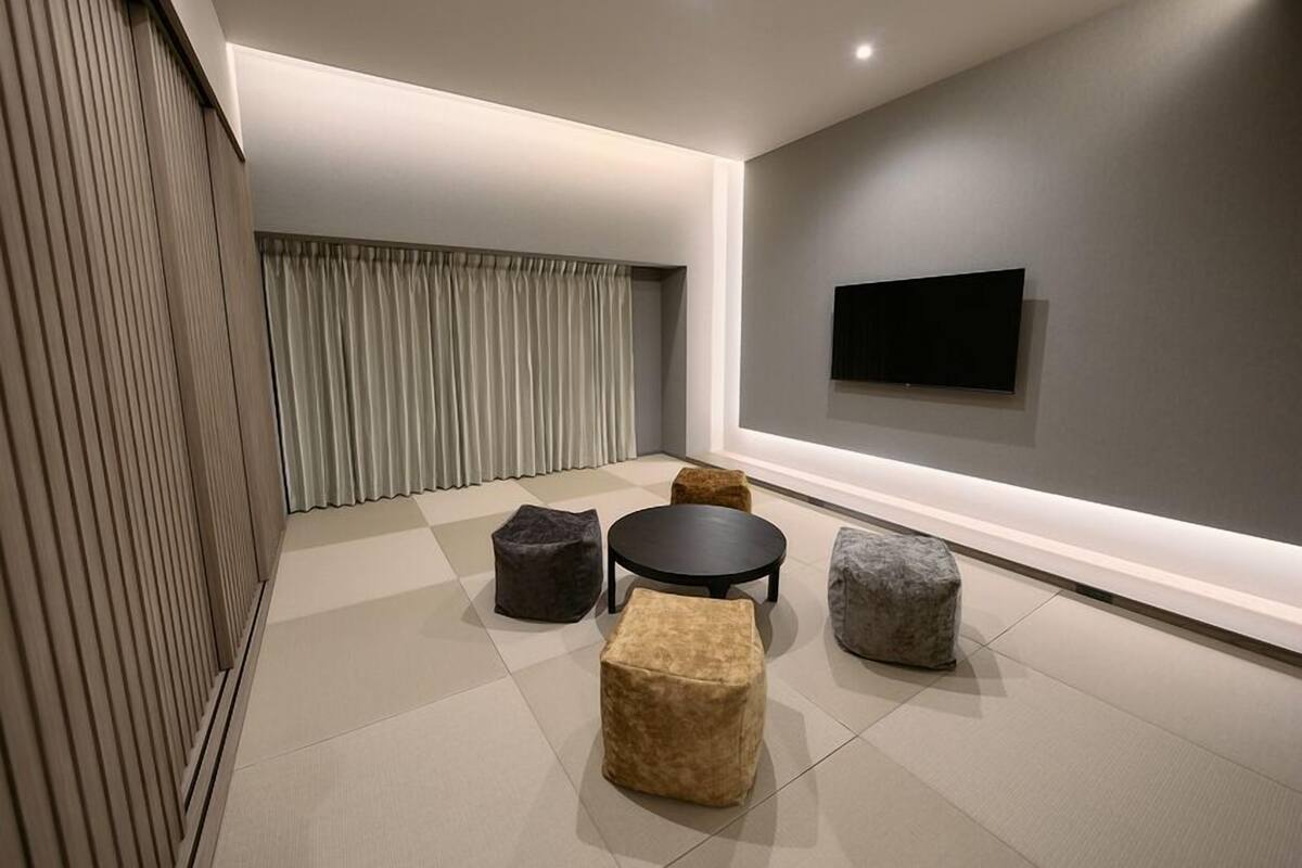 A modern living room with a flat-screen TV mounted on the wall, a round coffee table, and four ottomans in different colors.