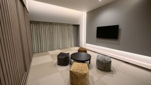 A modern interior with a flat-screen TV mounted on the wall, a round table, and four square ottomans in different colors. - fav HIROSHIMA STADIUM (Hiroshima)