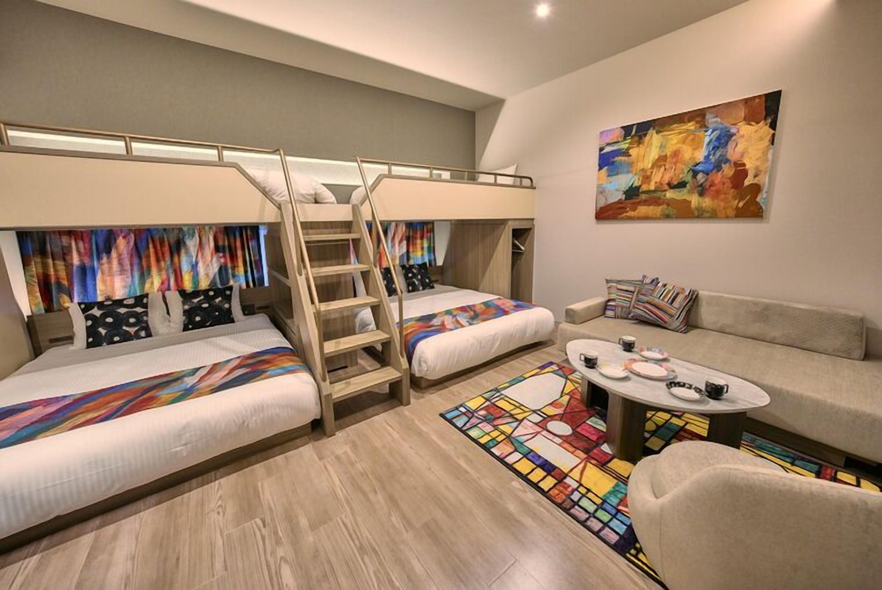 A modern bedroom with bunk beds, a sofa, a coffee table, and a colorful abstract painting.