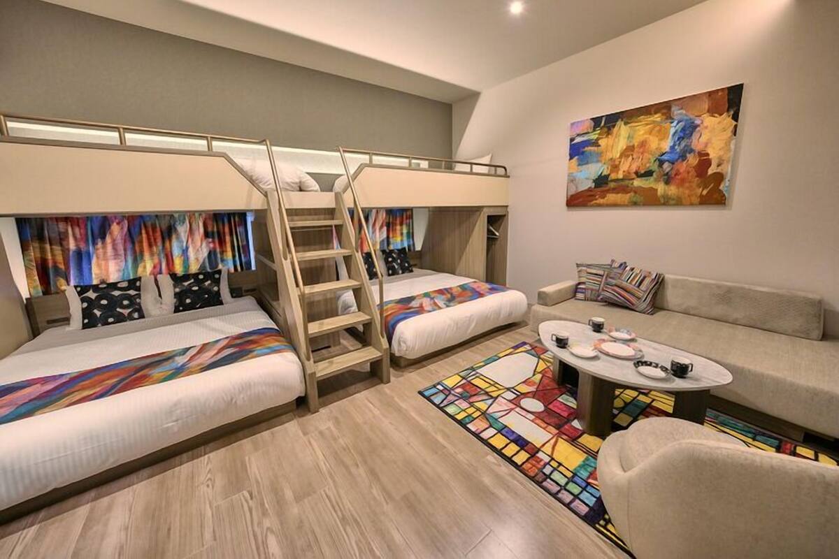 A modern bedroom with bunk beds, a sofa, a coffee table, and a colorful abstract painting.