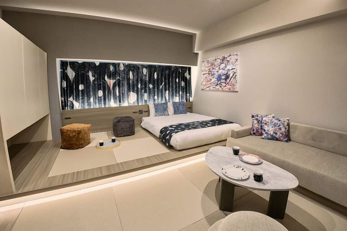A modern hotel room with a bed, sofa, coffee table, and artwork.