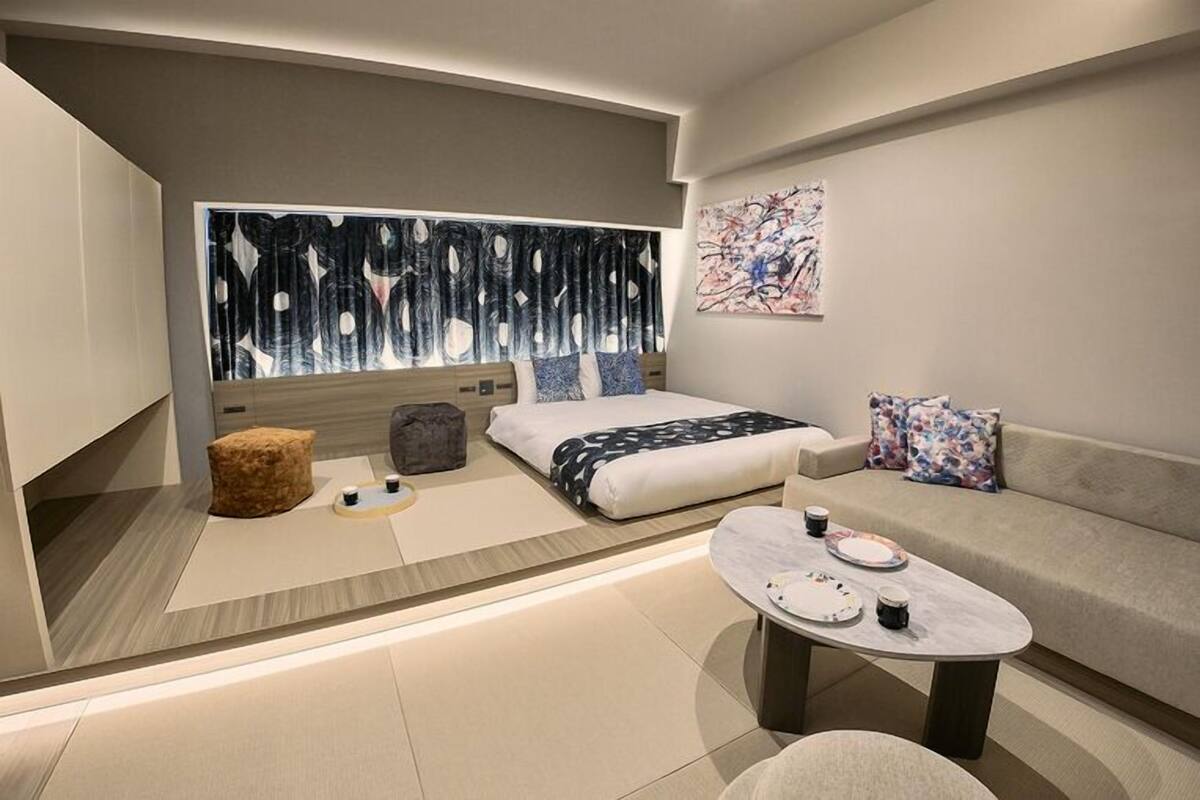 Una habitación de hotel moderna con cama, sofá, mesa de centro y obras de arte.