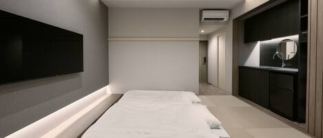 A modern hotel room with a large bed, a TV mounted on the wall, a mirror above the sink, and a walk-in closet.