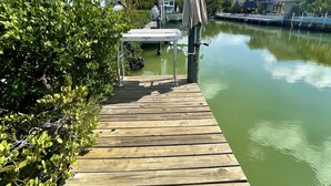 A wooden dock leading to a marina with boats, a covered table, and a palm tree. - Tropical Dream Vacation with 3 bdrm/2 baths, pool & dock - On Sombrero Beach Rd! (Marathon)