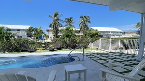 A poolside area with lounge chairs, a small table, and a view of a swimming pool and palm trees. - Tropical Dream Vacation with 3 bdrm/2 baths, pool & dock - On Sombrero Beach Rd! (Marathon)