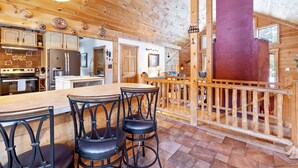 Interior de una cabaña de madera con cocina, comedor y una escalera.