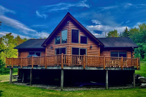 A log cabin with a balcony and a covered deck, surrounded by a natural landscape. - Cozy Vermont Log Cabin Chalet Only Minutes from Jay Peak (Montgomery)