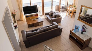 A modern living room with a sofa, TV, and a dining area with a table and chairs. - Villa Oleander - 4 bedroom Villa with Private Heated Pool, Hot Tub, Stunning Views (Paphos)