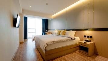 A modern hotel room with a large bed, bedside tables, a flat-screen TV, and a large window with curtains.
