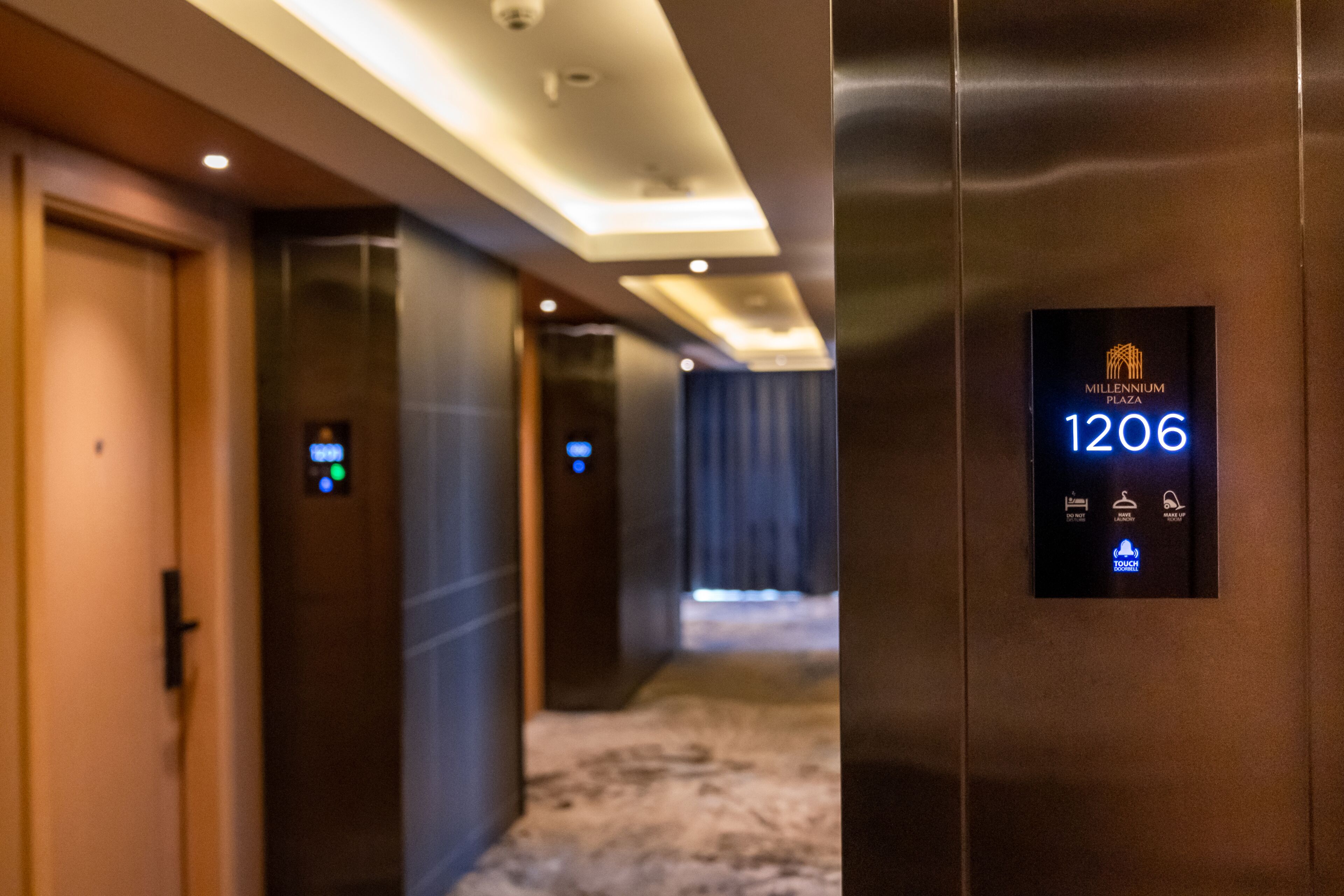 A hallway with a digital elevator display showing floor 1206, a touch panel, and a door with a lock.
