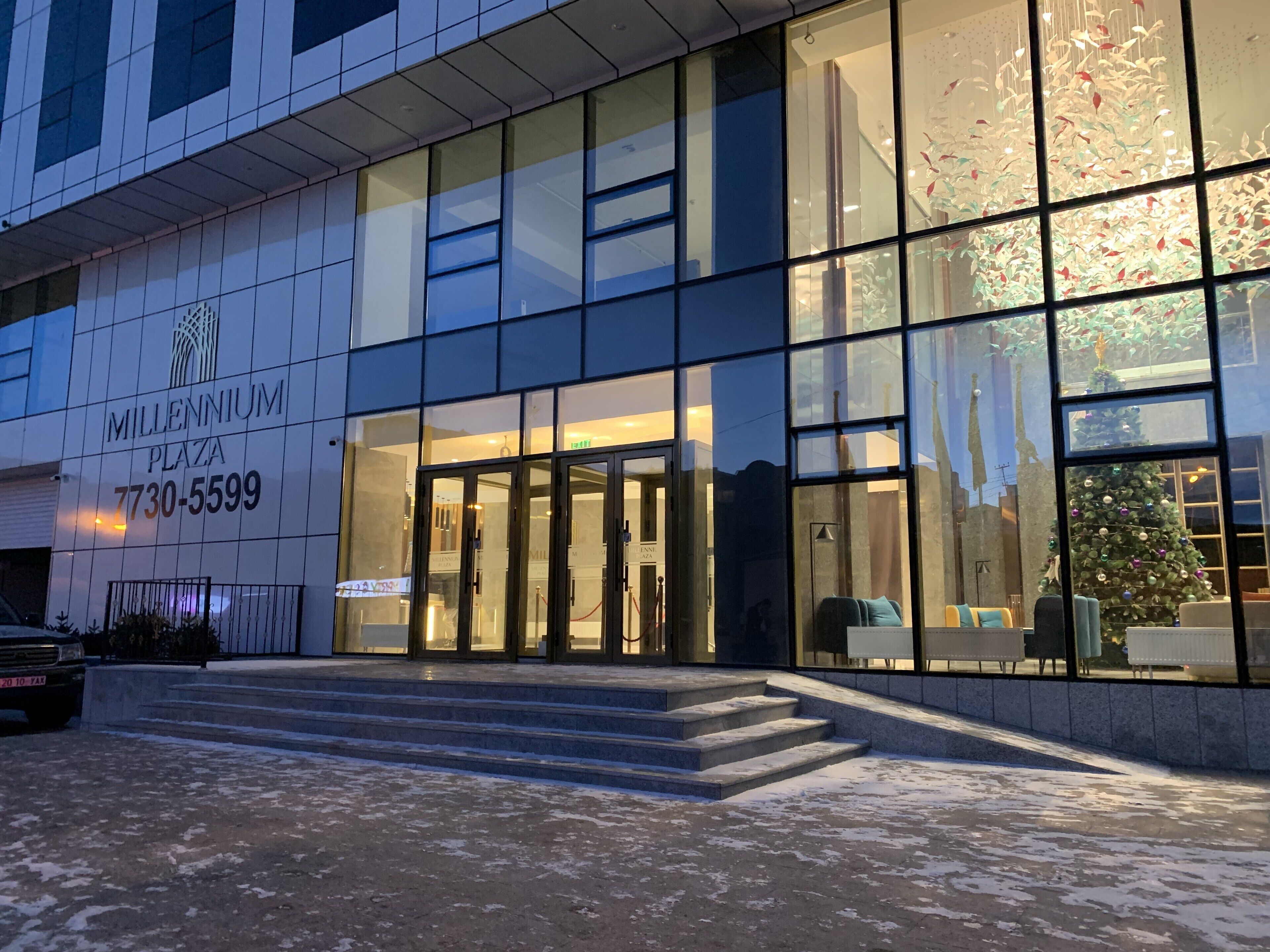 Een modern gebouw met een glazen gevel, een duidelijke ingang met glazen deuren, en een trap die naar de ingang leidt.