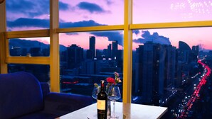 Ein Zimmer mit Blick auf die Stadt, ein Sofa, ein Tisch mit einer Flasche und Gläsern sowie Vorhänge.