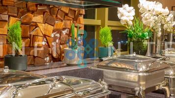 A buffet setup with covered food stations, potted plants, and a decorative wall.