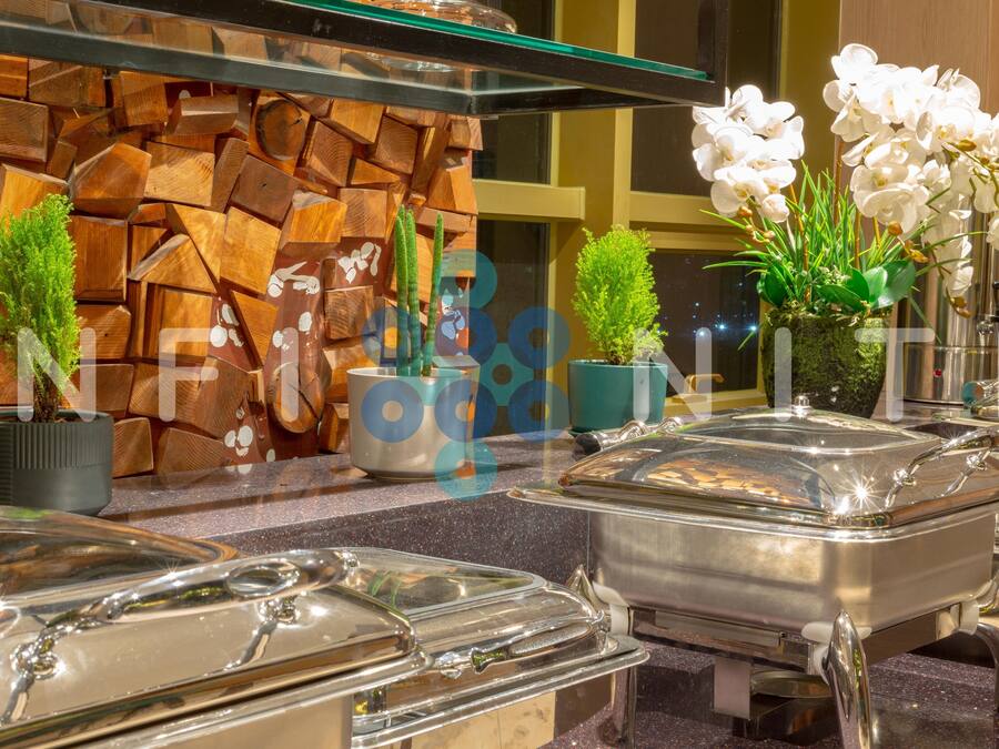 Montaje tipo buffet con estaciones de comida cubiertas, plantas en macetas y una pared decorativa.
