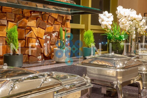 Montaje tipo buffet con estaciones de comida cubiertas, plantas en macetas y una pared decorativa.