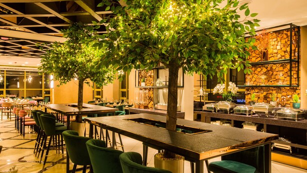 Ein Restaurant mit mehreren Tischen und Stühlen, einem geschmückten Baum mit Lichterketten und einer Steinsäule mit Regalen.