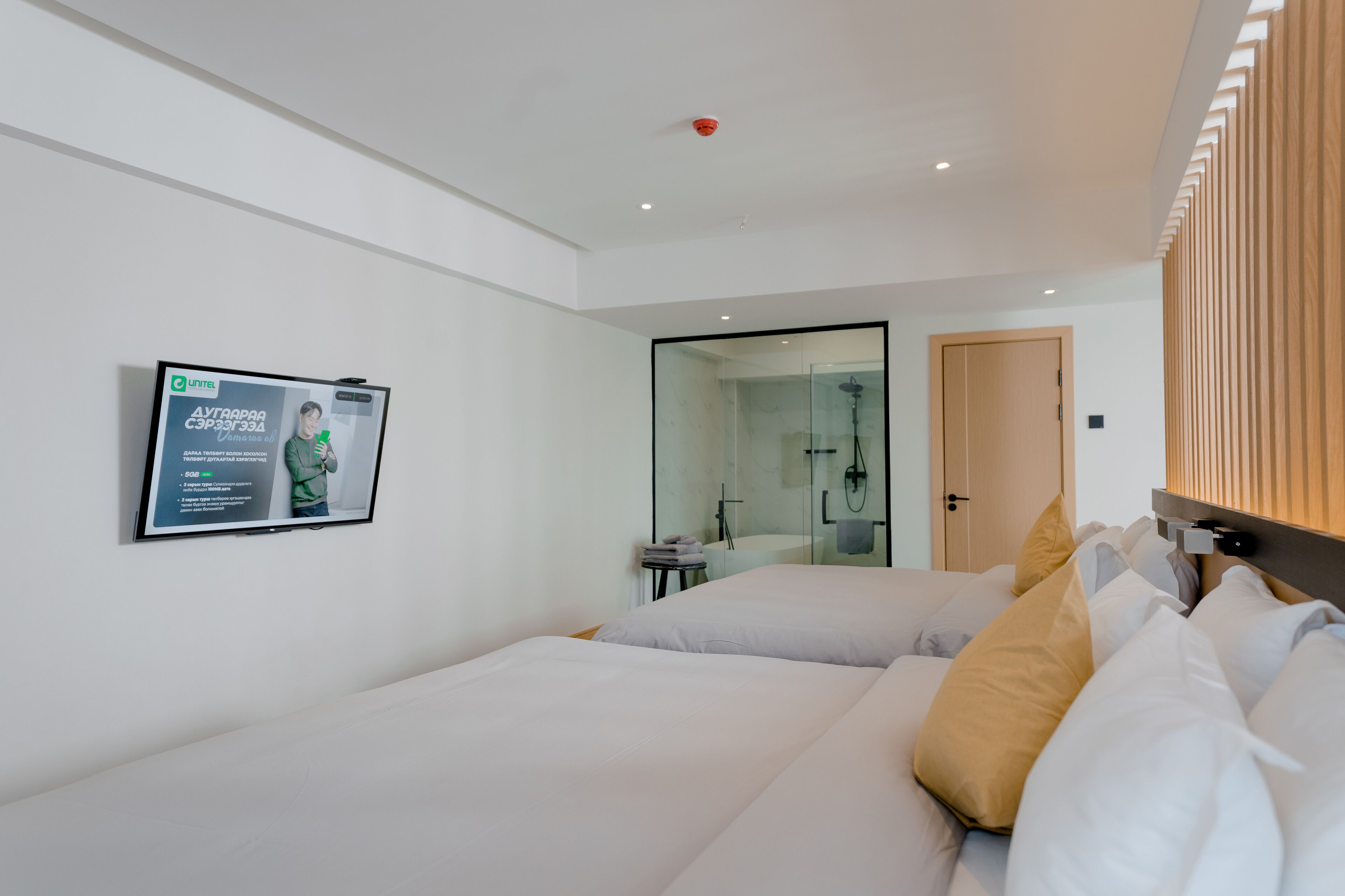 Una habitación de hotel moderna con dos camas, cabina de ducha de vidrio, televisor montado y pared de paneles de madera.