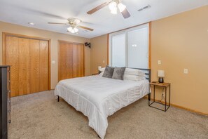 A bedroom with a bed, two wooden wardrobes, a ceiling fan, and a window. - Fenced Patio W/ POOL, Game Room, & Home Gym! (Wichita)