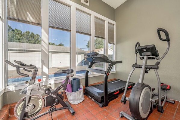 A home gym with exercise equipment including a stationary bike, elliptical, treadmill, and weights. - Fenced Patio W/ POOL, Game Room, & Home Gym! (Wichita)