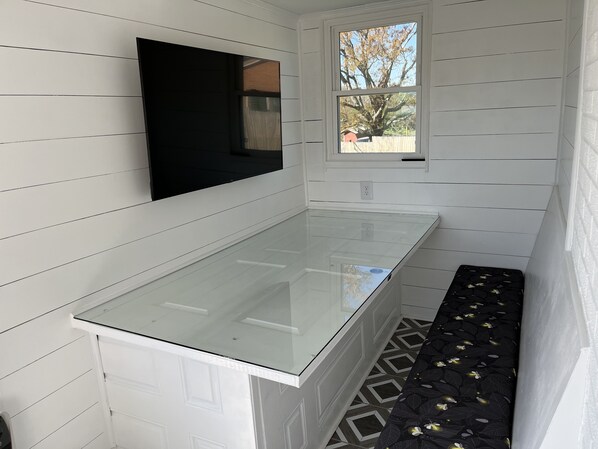 A bathroom with white paneled walls, a glass shower enclosure, a window with a view of trees, and a patterned floor.