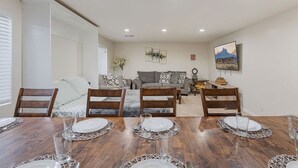 Een eetgedeelte met een houten tafel gedekt voor vier personen, omringd door houten stoelen. Achterin staat een bank en een bijzettafeltje met decoratieve objecten.