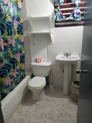 A small bathroom with a toilet, sink, and shower curtain. - Seascape Apartment (Negril)
