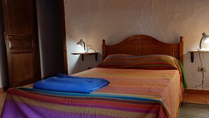 Una cama individual con una colcha a rayas de colores, dos lámparas de noche y un cabecero de madera.