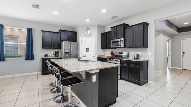 A modern kitchen with dark cabinets, a central island with bar stools, and a microwave. - Comfortably spacious home with a private pool, spa, and arcade. (Davenport)