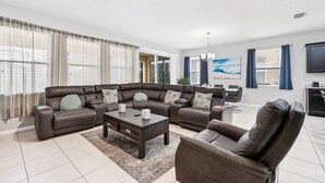A modern living room with a sectional sofa, a coffee table, and a TV. - Comfortably spacious home with a private pool, spa, and arcade. (Davenport)