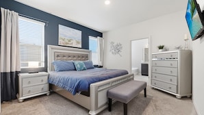A bedroom with a bed, nightstands, a dresser, a bench, and a TV mounted on the wall. - Comfortably spacious home with a private pool, spa, and arcade. (Davenport)