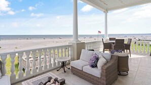 Un espacio al aire libre techado con vistas a la playa, que incluye un sofá, sillas y una mesita.