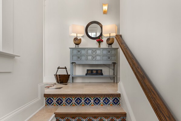 A staircase with a blue console table, two wall-mounted lamps, a mirror, and a small wooden chair.