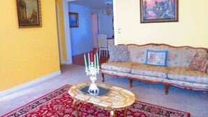 A living room with a floral sofa, a red patterned rug, a table with a glass top, and two paintings on the walls.