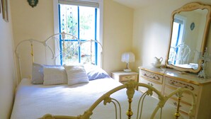 A bedroom with a bed, a dresser, a mirror, and a window with blue shutters.