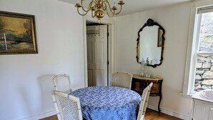 A dining room with a round table, four chairs, a chandelier, a mirror, and a painting on the wall.