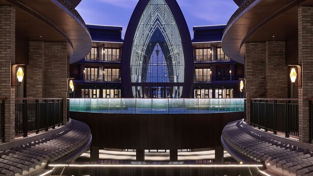 Un edificio moderno con un atrio centrale, una vasca riflettente e una facciata in vetro ad arco particolare.