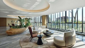 Un'ampia hall con design moderno, caratterizzata da una pianta grande, sedute confortevoli e ampie finestre con vista esterna.