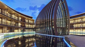 Un hotel moderno con facciata in vetro curvo, numerosi balconi e una piscina a specchio.