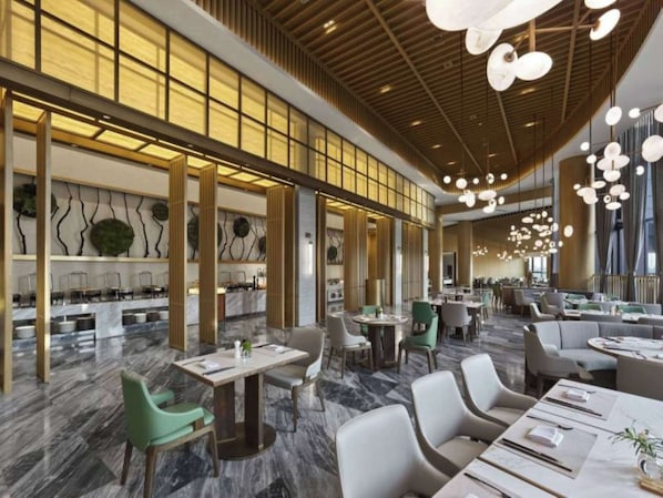 A spacious hotel lobby with marble flooring, modern furniture, and a high ceiling with hanging lights.