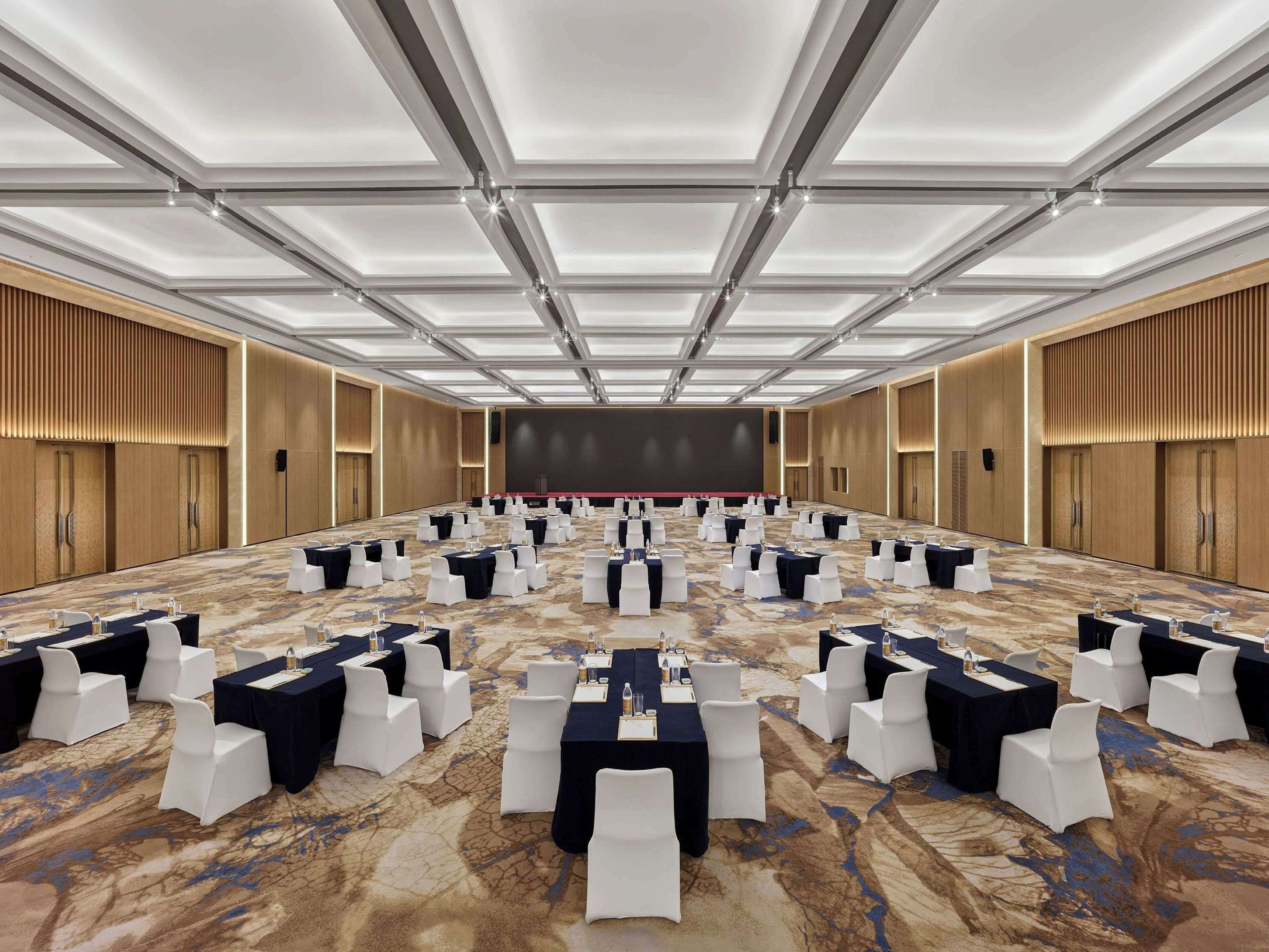 Un amplio salón de conferencias con techo alto, varias mesas con manteles blancos y negros, y una alfombra estampada.