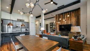 Une cuisine moderne équipée d’appareils électroménagers en acier inoxydable, un coin repas avec une table en bois et un salon doté d’un téléviseur et de sièges confortables.